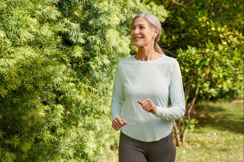 Person jogging along a grassy, tree‑lined path while wearing athletic clothing.