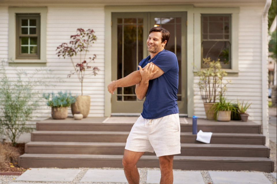 Person in blue shirt stretching arms outdoors on a front porch.