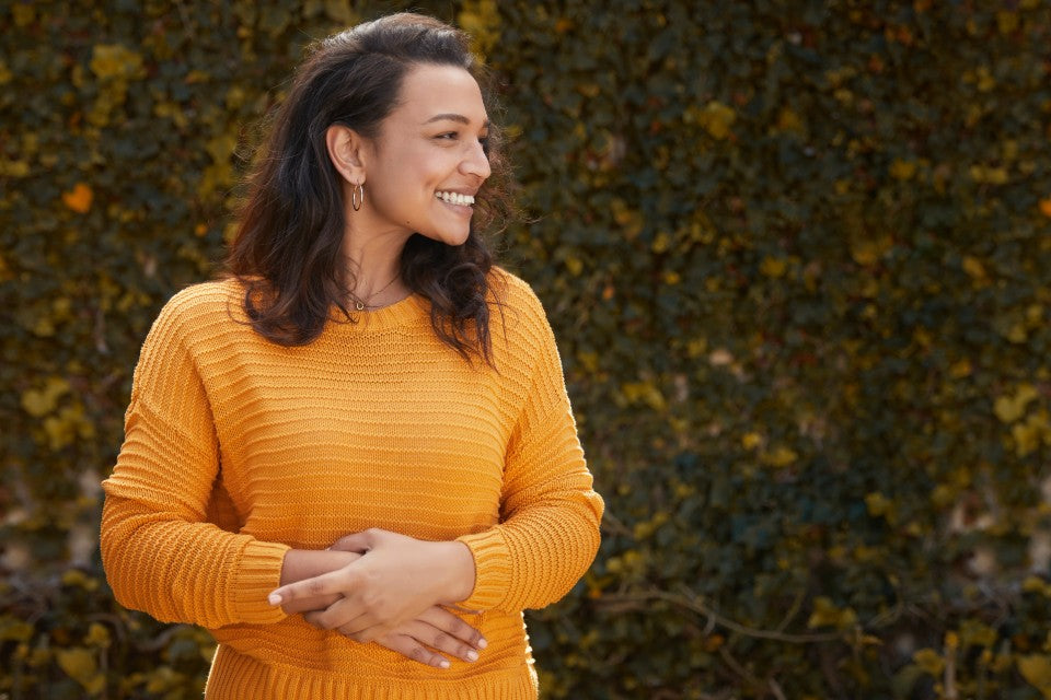 Person in yellow standing outdoors with hands resting on their stomach.