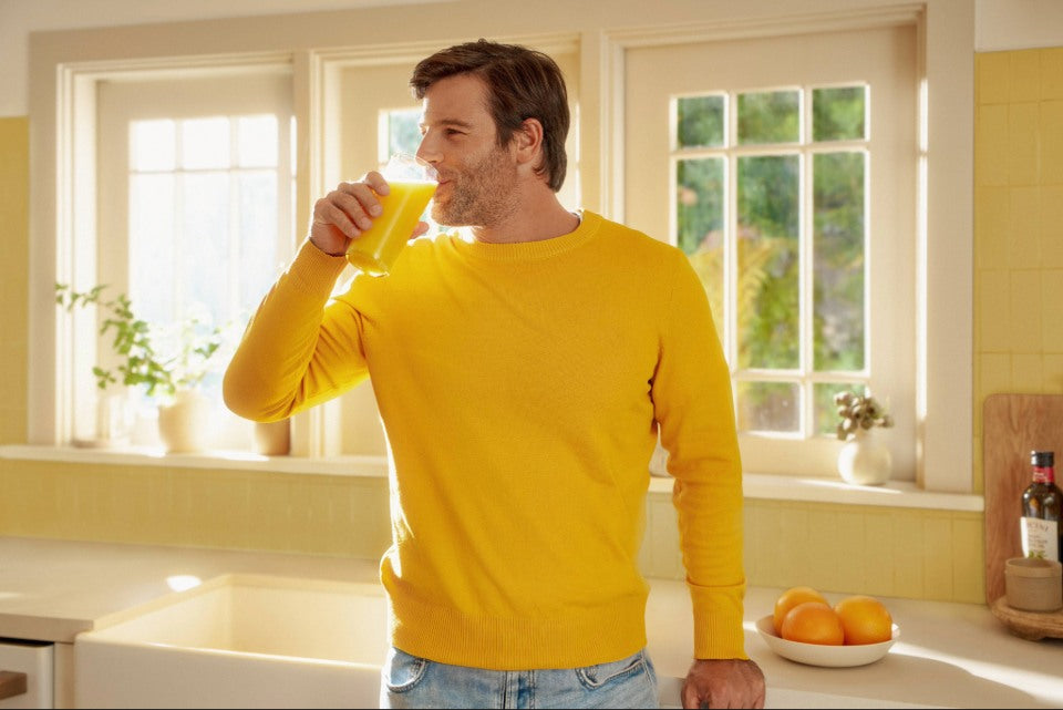 Person drinking a glass of orange juice in a bright kitchen, representing vitamin C intake and energy.
