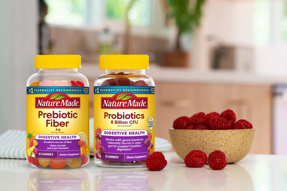 Two bottles of Nature Made prebiotic fiber and probiotics on a kitchen counter with a bowl of raspberries.