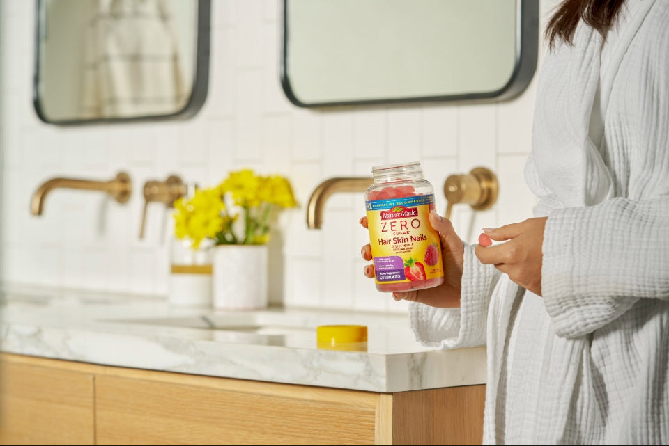 Person holding Nature Made Zero Sugar Hair, Skin & Nails gummies on a bathroom vanity.