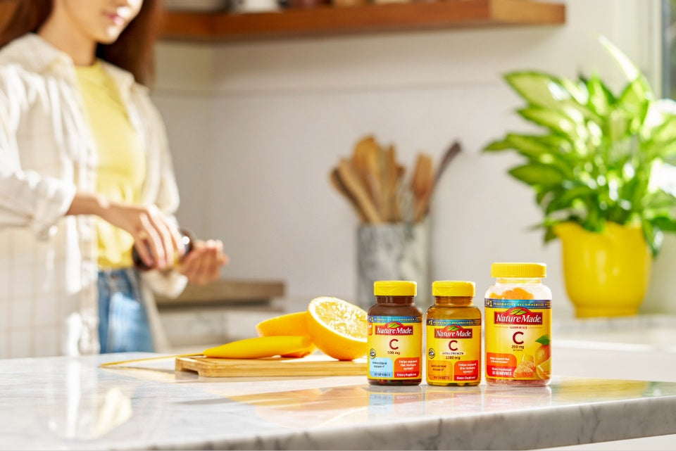 Nature Made vitamin C supplements displayed on a kitchen counter with fresh oranges.