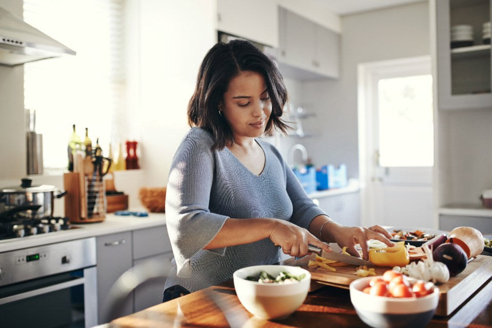 Person chopping fresh vegetables on a wooden cutting board in a modern kitchen.