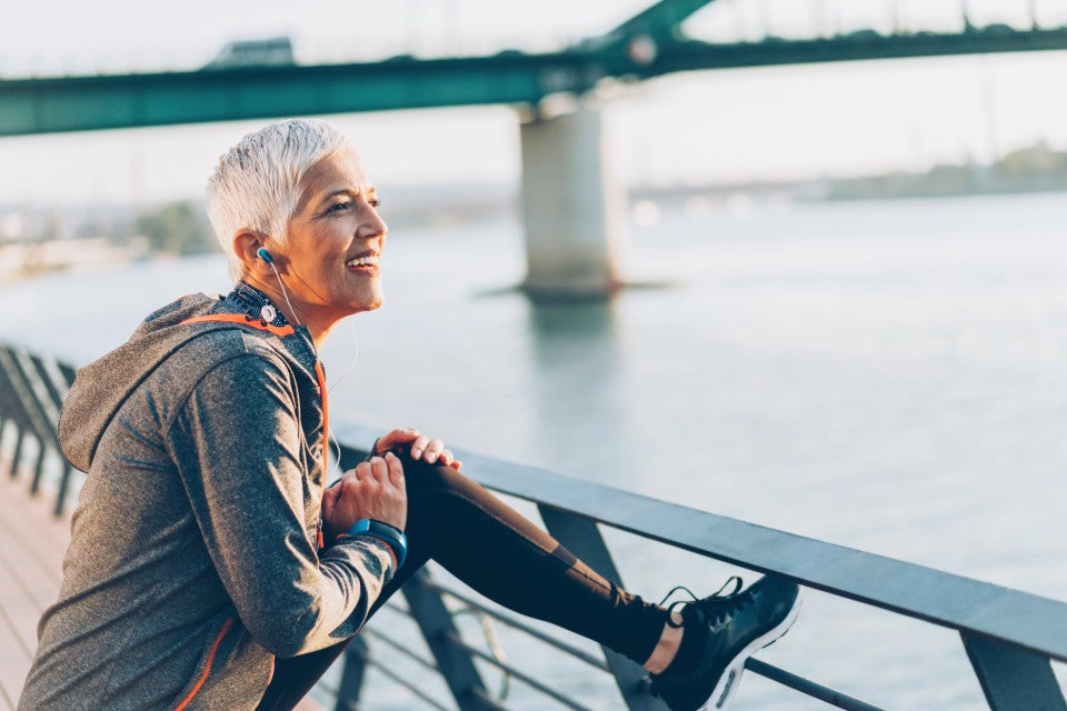 Active person stretching outdoors by a riverside bridge, wearing athletic gear.
