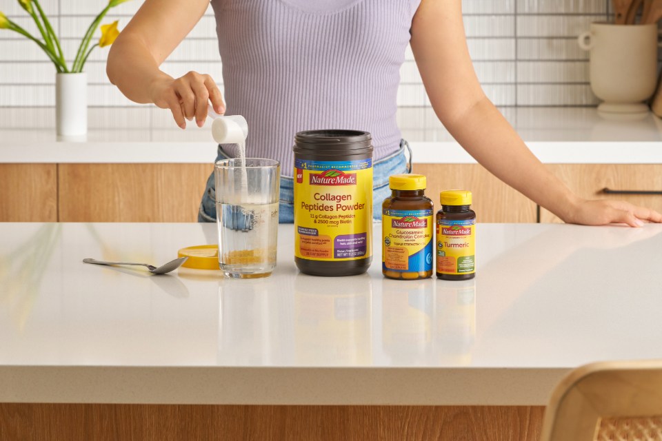 Person preparing a glass of water with Nature Made Collagen next to Glucosamine and Turmeric supplements displayed on a kitchen counter.
