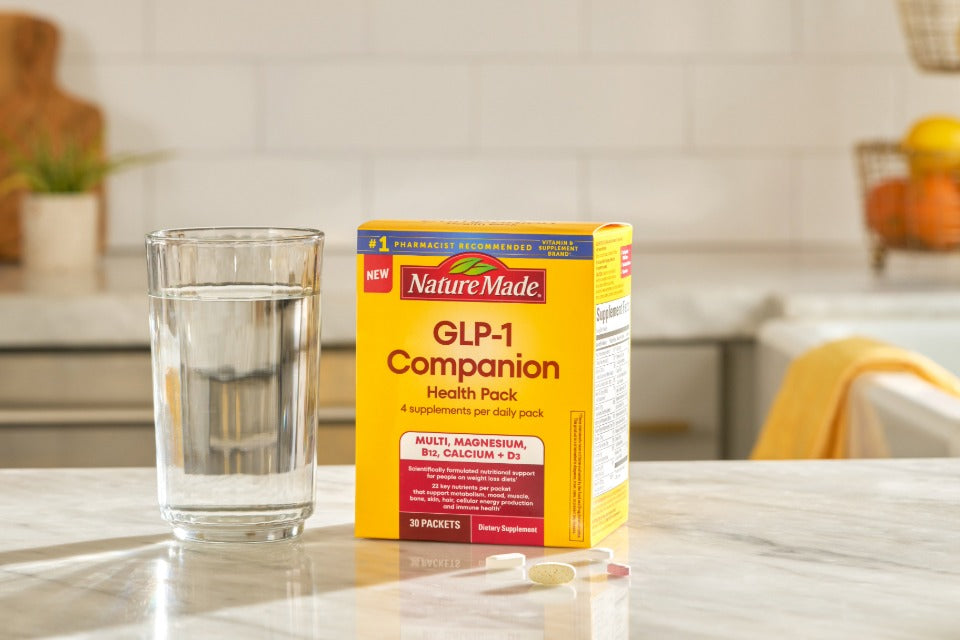 Nature Made GLP-1 Companion Health Pack with supplements and a glass of water on a kitchen counter.
