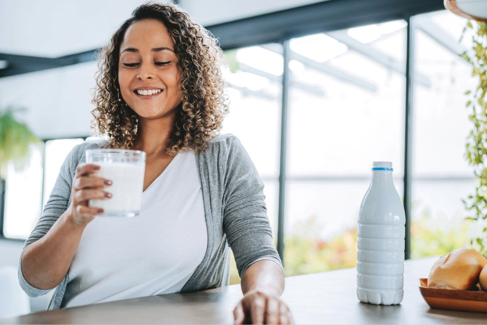 Person sitting at a table holding a glass of milk with a milk bottle.